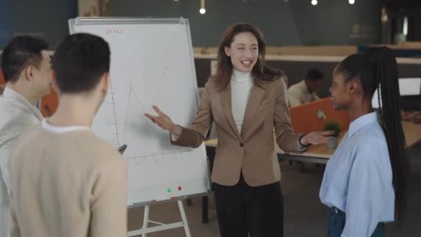 Heureux groupe multiethnique souriant de gens d'affaires applaudissant au jeune directeur de leader après la présentation sur tableau à feuilles mobiles dans la salle de bureau. Affaires, finance, ventes, succès. — Video