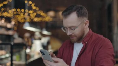 Neşeli adam kafede çalışırken mesajlaşmak için akıllı telefon kullanıyor..