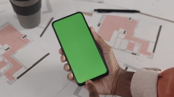 Man architect of ontwerper tikken smartphone met groene scherm mock-up chroma sleutel op de werkplek, bovenaanzicht. Lijntekening plattegrond op een achtergrond. Sluiten.. — Stockvideo
