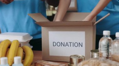 Gönüllüler depodaki karton kutunun içine malzeme koyuyorlar.