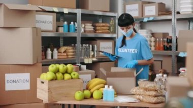 Maskeli ve eldivenli bir kadın yemek bankasında tablet kullanıyor.