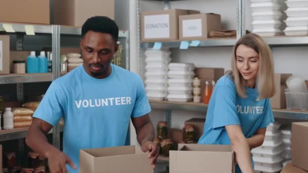 Dos voluntarios diversos empacando cajas de donación — Vídeos de Stock