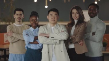 Ofis odasında durup kolları bağlı kameraya bakan mutlu iş adamlarının portresi. Çok ırklı profesyonel çalışanlar takım portresi ve liderlik için birlikte poz veriyorlar..