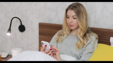 Yatakta oturmuş sohbet eden ya da akıllı telefondaki sosyal ağları kaydıran bir kadın..