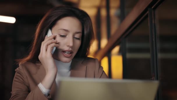 Frau telefoniert mit Handy, während sie mit Laptop im Café sitzt — Stockvideo