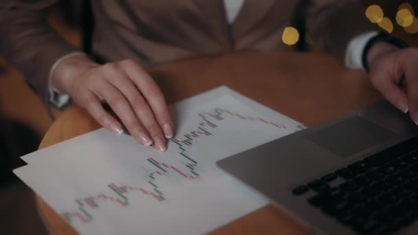Händlerin lernt Finanzkursdiagramm. Geschäftsfrau tippt auf Laptop und checkt Diagramme auf Papier, während sie im modernen Café sitzt. Aus nächster Nähe. Finanzierungskonzept. — Stockvideo