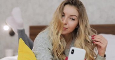 Bir kadın evde yatarken gülümsüyor ve akıllı telefon kamerasına bakıyor..