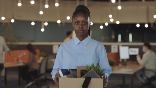 Retrato de una desempleada afroamericana emloyee despedida del trabajo. Mujer joven molesta con la caja llena de cosas en las manos mirando a la cámara. En interiores. Disparando desde el trabajo. Crisis y negocios. — Vídeo de stock