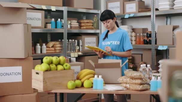 Voluntária feminina usando prancheta enquanto trabalhava no banco de alimentos — Vídeo de Stock