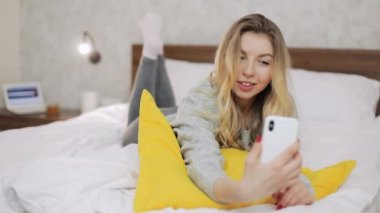 Evdeki akıllı telefon kamerasına poz veren bir kadın. İnsanlar ve teknoloji kavramı.