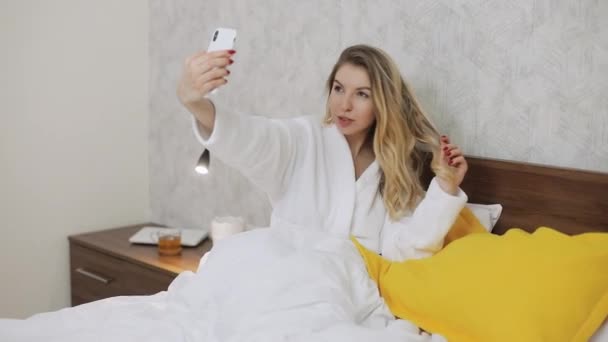 Nő csinál szelfi fotó és videó az ő smartphone elülső kamera az ágyban. — Stock videók