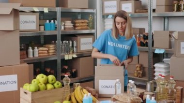 Güzel bir kadın depoda bağış için yiyecek kutuları hazırlıyor.