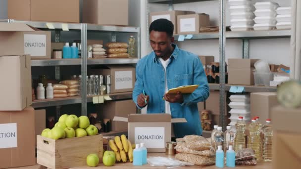 Africano americano homem escrevendo na área de transferência entre banco de alimentos — Vídeo de Stock