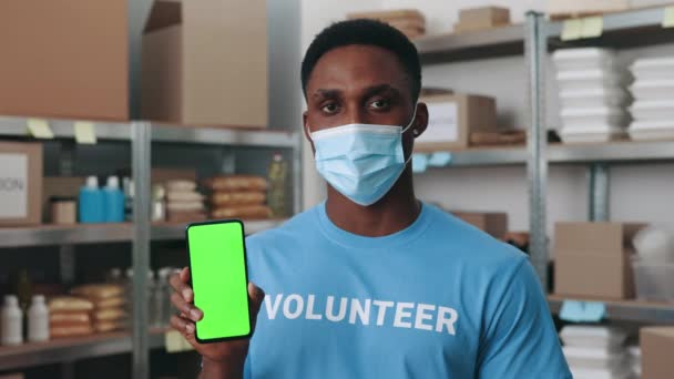 Hombre con máscara sosteniendo móvil con pantalla verde en el banco de alimentos — Vídeos de Stock