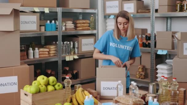 Beautiful woman preparing food boxes for donation at storage — Video