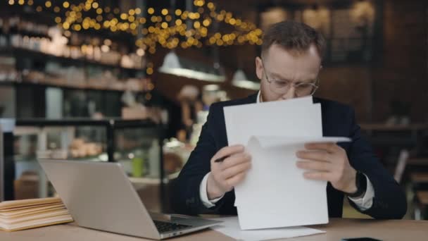 Empresario mirando a través de los papeles, frunciendo el ceño con el ordenador portátil, fallando tarea urgente. — Vídeos de Stock
