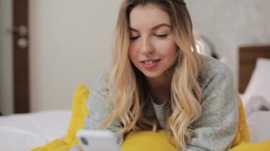 Yatak odasında uzanmış cep telefonuyla sohbet eden bir kadın..