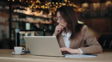 Laptopta yazan ve kafede öksüren bir kadın.