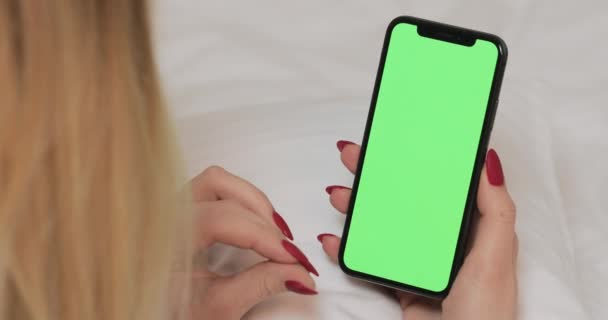 LVIV, UKRAINE- 5 березня 2022: Жінка тримає смартфон з зеленим порожнім екраном на ліжку вдома.. — стокове відео