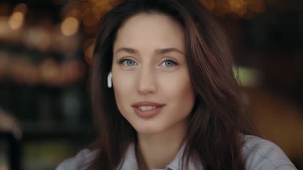 Γυναίκα με ακουστικά χαμογελώντας και κοιτάζοντας την κάμερα στο καφέ — Αρχείο Βίντεο
