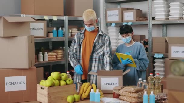 Pracownicy społeczni w maskach do twarzy pakujący pudełka darowizn — Wideo stockowe