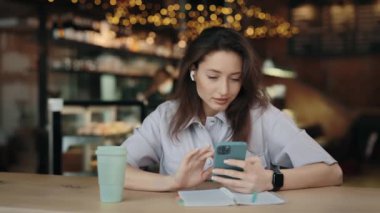 Charming woman in earphones using smartphone at cafe