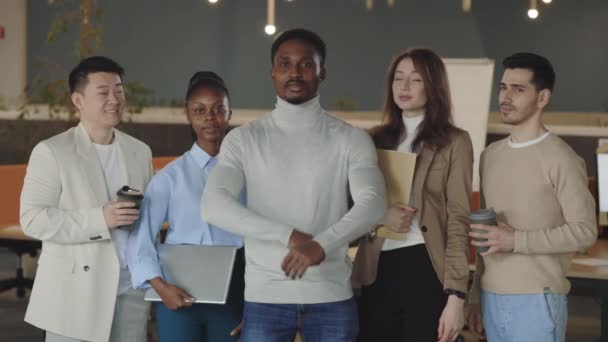 Multiracial company staff standing and crossing hands in office. Group of successful mixed workers with ther boss looking to camera and smiling. Concept of team portrait. — стоковое видео