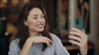 Neşeli genç bir kadın, rahat bir kafede dinlenirken selfie çekmek için modern akıllı telefonu kullanıyor. İnsan kavramı, eğlence ve aletler..