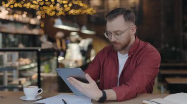 Kafede çalışırken tablette yazan yetenekli programcının belden portre görüntüsünü yükselt. Adam hafif gülüşlü bir alet kullanıyor. Teknoloji ve insanlar kavramı