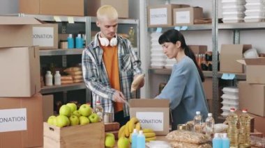 Genç erkek ve kadın gönüllüler bağış kutularını paketlemek için hayır kurumunda çalışıyorlar. Gündelik giysiler içinde beyaz bir erkek ve kadın yardıma ihtiyacı olan insanlara yardım etmek için birlikte çalışıyorlar..