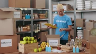 Yemek deposundaki envanter sırasında mavi gönüllü tişörtlü beyaz adam panoya yazı yazıyor. Gönüllü olmak, teknoloji ve bağışta bulunmak.