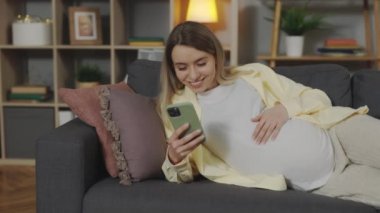 Pregnant woman relaxing on sofa with mobile in hands