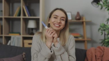 Elinde pozitif hamilelik testiyle kamerada konuşan bir kadın.