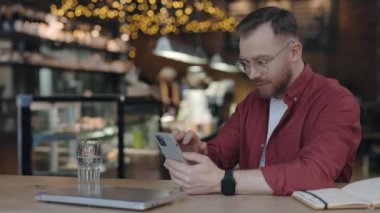 Adam kafede çalışırken mesajlaşmak için akıllı telefon kullanıyor..