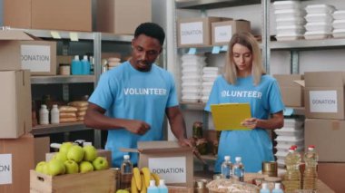 Kadın panoya yazı yazarken, erkek bağış kutusu hazırlıyor.