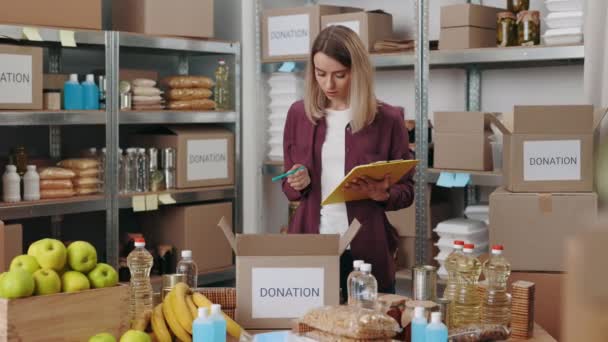 Young woman with clipboard volunteering at food bank — ストック動画