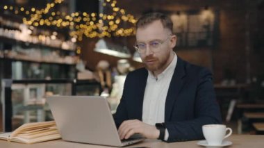 Kafede dizüstü bilgisayarla çalışırken kameraya bakan işadamının portresi.