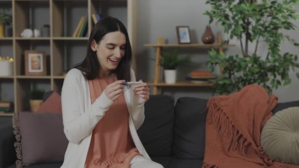 Γυναίκα κάθεται σε καναπέ με θετικό τεστ εγκυμοσύνης στα χέρια — Αρχείο Βίντεο