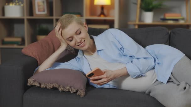 Усміхнена жінка дивиться відео по телефону вдома — стокове відео