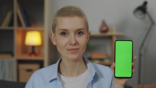 Smiling woman holding smartphone with green screen at home — Wideo stockowe