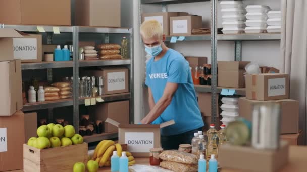 Man in face mask preparing donation boxes at food bank — Stock video