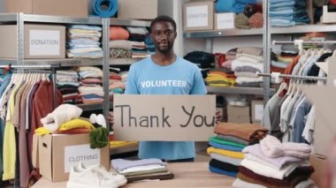 Çeşitli erkek gönüllülerin portre görüntüsü. Dolap afişi tutarken, teşekkür cümlesiyle ve gülümseyerek kameraya bakarken. Arkasında eşyalar olan raflar. İnsani yardım kavramı.