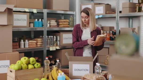 Woman packing boxes with food for donation at warehouse — Video