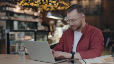 Modern kafede okuyan, klavyede yazan, dizüstü bilgisayarını kullanan bir adam..