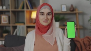 Evde boş yeşil ekranlı telefonu tutan Arap kadın.