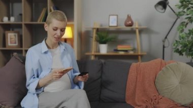 Evde online alışveriş yapmak için kredi kartı ve telefon kullanan bir kadın.