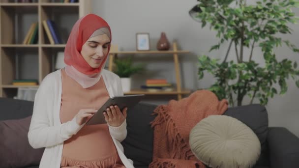 Müslüman hamile kadın elinde tabletle kanepede dinleniyor. — Stok video