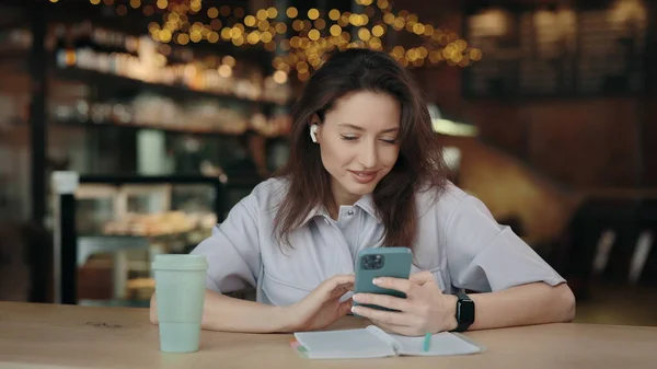 Kafede akıllı telefon kullanan kulaklıklı çekici bir kadın.