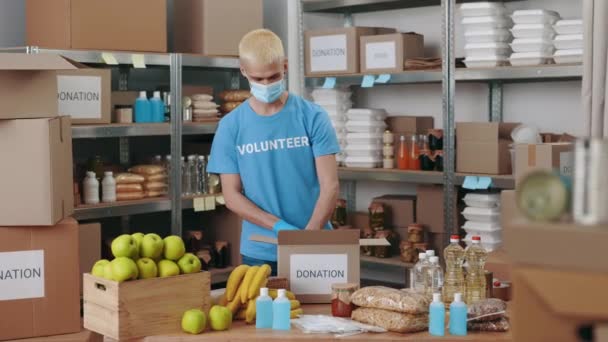 Pracownik banku żywności w masce do twarzy przygotowuje skrzynki darowizn — Wideo stockowe