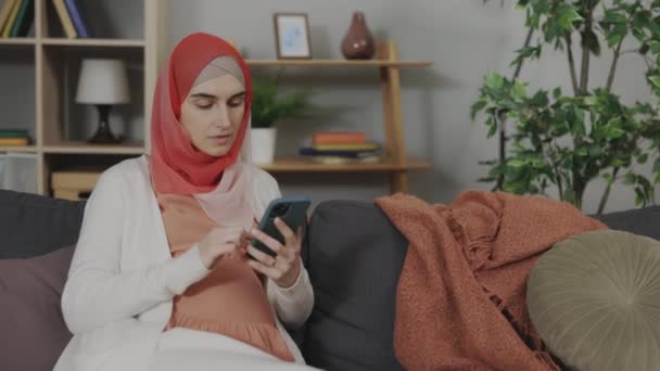 Gravid muslimsk kvinna med smartphone känner smärta i magen — Stockvideo